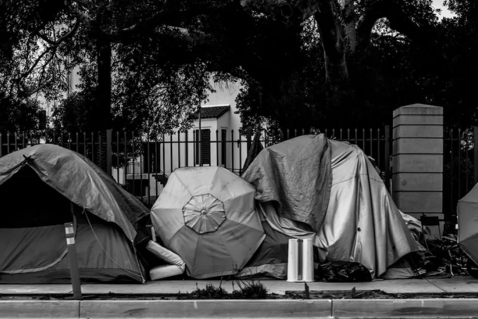 Black and white photo of row of tents set up against fence outdoors.